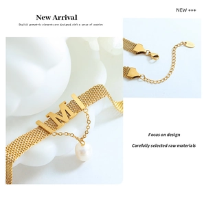 Macro view of gold mesh chain necklace featuring a letter M and natural pearl charm