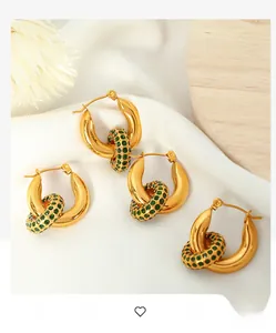 Detail of gold hoop earrings with green zircon pendants on white silk background