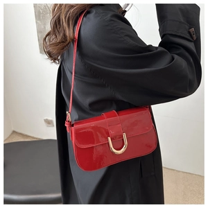 Red patent leather shoulder bag with gold horseshoe buckle worn by model