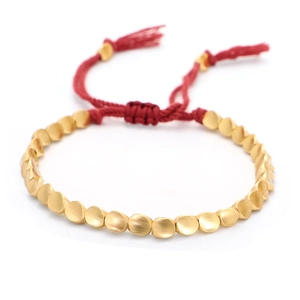 Detalle de pulsera de cordón rojo trenzado con cuentas de oro mate y cierre de borlas