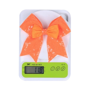 Sequin bow hair clip in bright orange shown on a scale for weight measurement detail