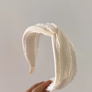 Detail of cream fabric knotted headband with rustic fringe edges shown in hand
