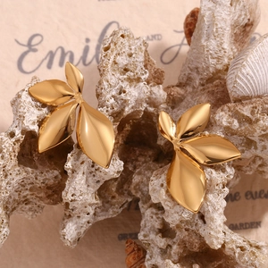 Macro shot of 18K gold-plated leaf stud earrings on a white coral stone background