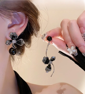 Detail of asymmetrical black flower earrings with sparkling crystals and drop pearls