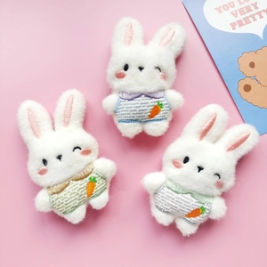 Three cute plush rabbit brooches in colorful striped outfits on a pink background