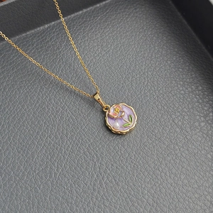 Baroque pearl necklace with a purple floral enamel pendant on a leather tray