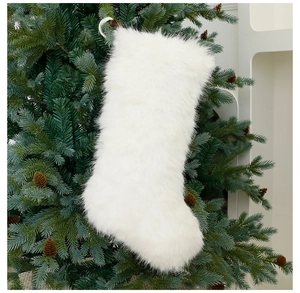 Detail of white faux fur Christmas stocking hanging on a festive tree with pine cones