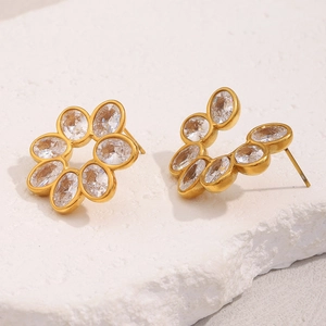 Macro view of gold flower earrings with oval zircons on white textured background
