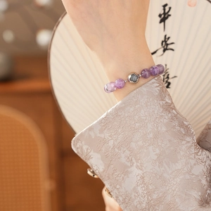 Detailed shot of amethyst bead bracelet with silver clover charm on wrist with folding fan