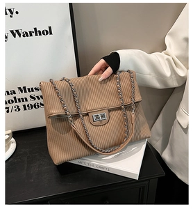 Detail of brown textured handbag with silver lock and metallic chain strap