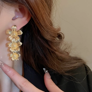 Detail of three-tier gold flower drop earrings with a brushed metallic texture