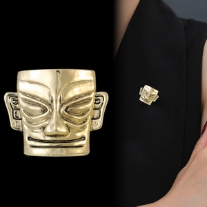 Detailed view of golden Sanxingdui style mask brooch on black suit lapel with vintage texture