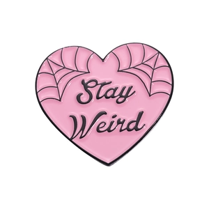 Pink heart-shaped metal brooch featuring black spiderweb pattern and Stay Weird text