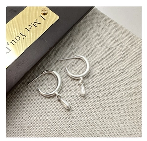 Macro shot of silver teardrop hoop earrings on textured beige linen background