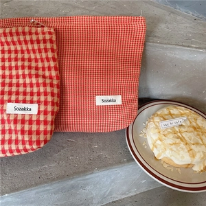 Detalle de neceseres de jacquard con cuadros rojos y pata de gallo con cremalleras metálicas