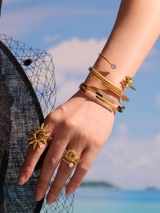 Detail of stacked gold-plated bracelets and zircon rings on a model against a sea background