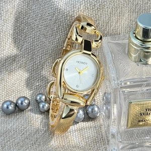 Detail of a gold horseshoe-case ladies' bangle watch with diamond accents on a linen background