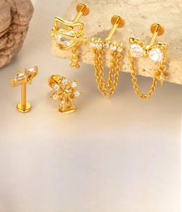 Detail of gold titanium labret studs featuring cat, bow, and chain designs with zircon inlay