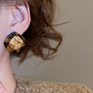 Macro detail of retro leopard print resin earrings with hammered gold inlay on ear