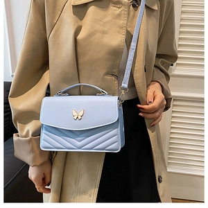 Blue crossbody bag with butterfly metal clasp and V-shaped quilting shown on model