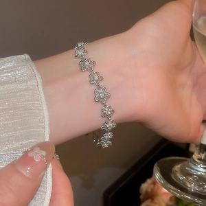 Silbernes Blumenarmband mit Zirkonia am Handgelenk einer Frau, die ein Glas Sekt hält