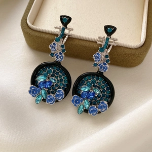 Dettaglio di orecchini vintage a forma di pipa con rose blu e cristalli petrolio