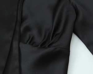 Detail of black satin shirt showing pleated texture and smooth drape on fabric surface