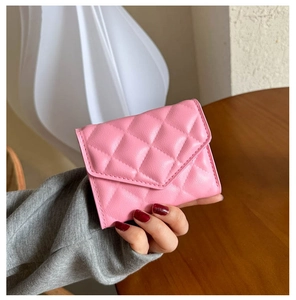 Detailed macro view of a pink quilted leather wallet held by hand in a cozy interior