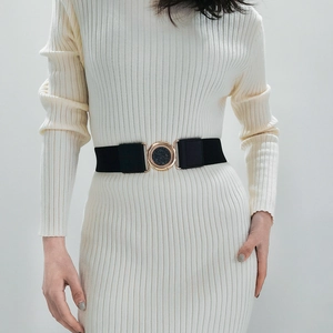 Detail of a black elastic waist belt with a round gold buckle on a cream knit dress