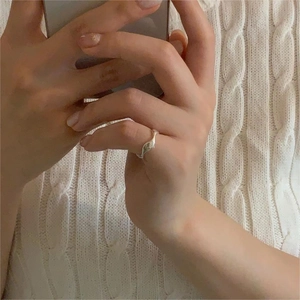 Close-up of wavy S925 sterling silver ring on hand with cream sweater background