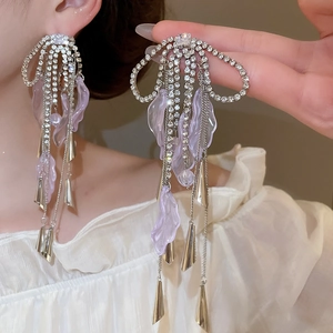 Close-up of sparkling bow tassel earrings with purple flower petals on model's ear