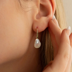 Baroque irregular pearl drop earrings with golden hook on a model's ear profile