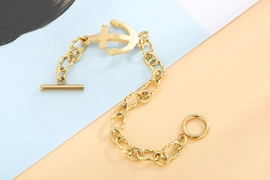 Detail of chunky gold anchor bracelet with toggle clasp on blue and orange background