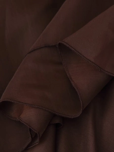 Dettaglio ravvicinato di tessuto chiffon marrone scuro con bordi a balze e cuciture