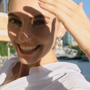 Close-up of golden bee hoop earrings with turquoise details on a model outdoors