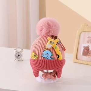 Detail of pink knitted baby hat with soft giraffe patches and large plush pom-poms