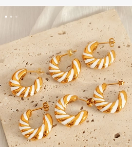 Artistic arrangement of gold and white enamel spiral C-shaped earrings on stone surface