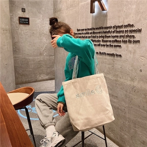 Close-up of smile embroidery on cream canvas tote bag with woven shoulder strap