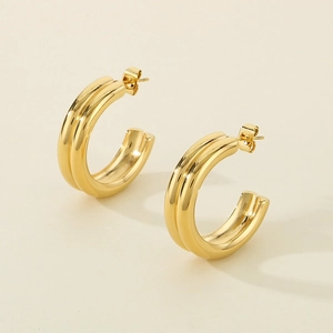 Close-up of polished gold C-shape stud earrings with minimalist metal texture on beige