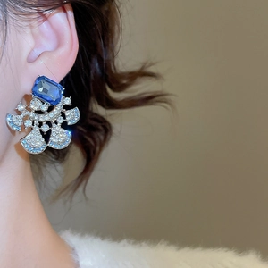 Macro side view of silver earrings featuring blue rectangular crystal and rhinestone fan