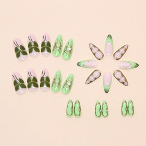 Detail of almond fake nails with emerald green butterflies, pearls and gold metallic patterns