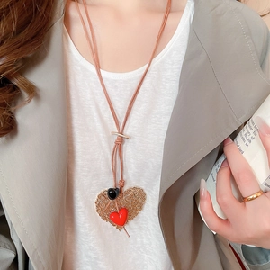 Detail of a large gold hollow heart pendant with a red heart on a brown leather cord