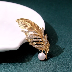 Macro shot of gold feather brooch featuring fine textures, sparkling crystals and a pearl