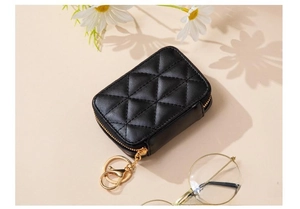 Detail of black quilted pouch with gold zipper and swivel hook on beige background