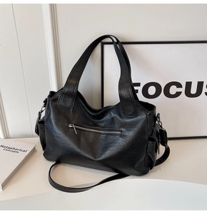 Detail of black leather tote bag with metal zipper and fine textured finish on white surface