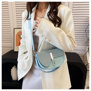 Light blue crossbody bag with textured patchwork and silver rotary lock on white blazer