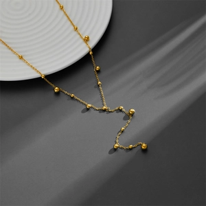 Minimalist gold Y-shaped necklace with multiple golden beads on a white textured dish