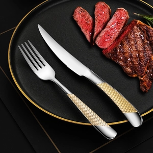 Luxury stainless steel steak knife and fork set with gold handles on a black dinner plate