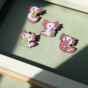 Détail de quatre broches en émail axolotl rose avec snacks sur fond vert clair
