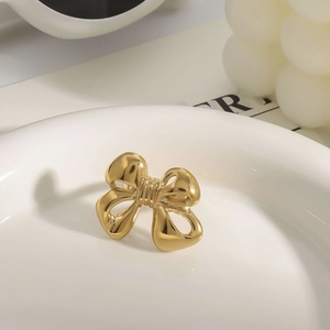Close-up of a polished gold bow necklace displayed on a ceramic plate with decor